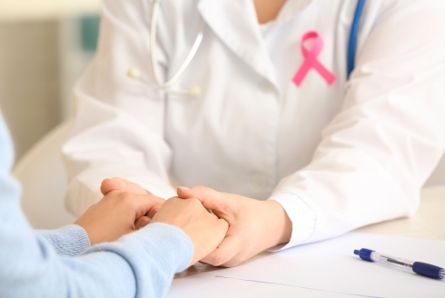 medical person in white jacket with pink ribbon holding hands of patient