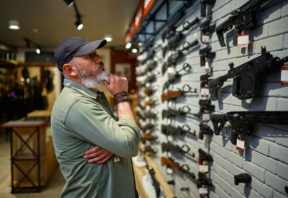 man browses display of firearms in a store (Adobe stock photo)