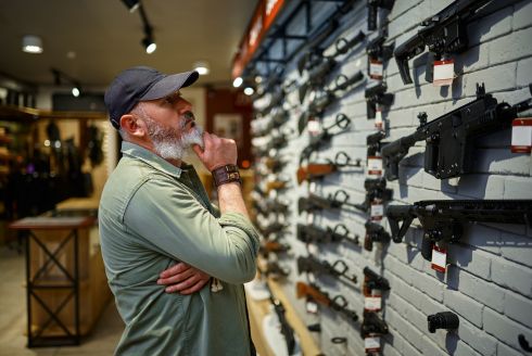 man browses display of firearms in a store (Adobe stock photo)