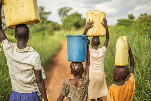 children carry gas cans and buckets atop their heads through field