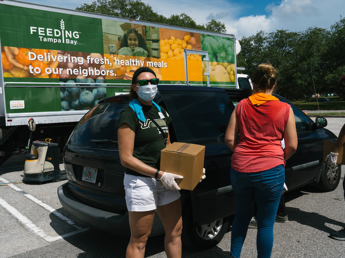 woman in mask carrying box near Feeding Tampa Bay truck