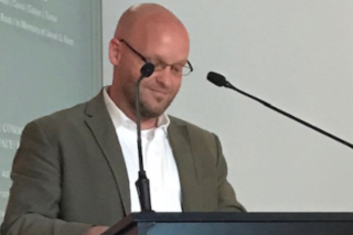 Picture of Adam Carter standing behind a lecture podium with microphones