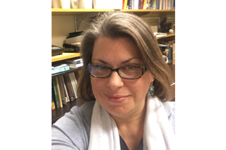 Image shows headshot of alumna Heather Fox smiling into the camera in front of rows of bookshelves filled with books.