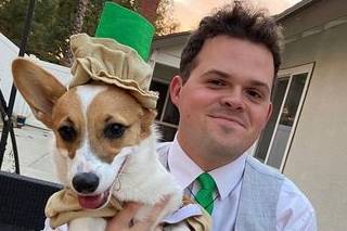 Headshot of Patrick Templeton smiling into camera and holding a corgi wearing a hat