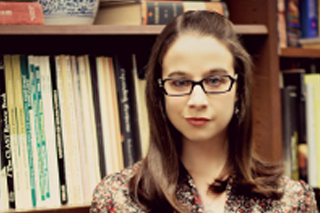 Image shows Christine M. Lasek smiling at the camera in front of wooden bookcases filled with books