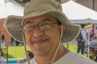 Headshot of Aby Boumarate smiling into the camera wearing a hat
