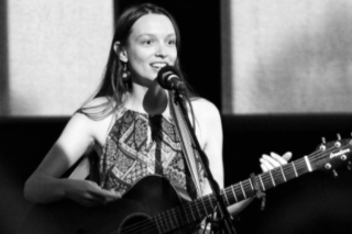 Picture of Erin Olds standing behind a microphone and holding a guitar