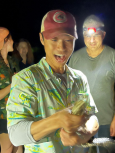 man excitedly holding reptile with 3 people around him outdoors at night 