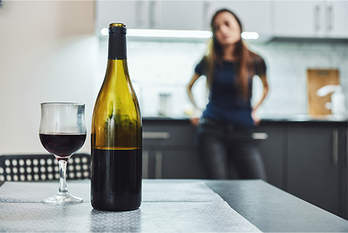 A woman looking at the wine glass and bottle on the table