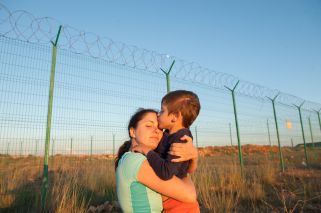 migrant mother holding child near a wire fence