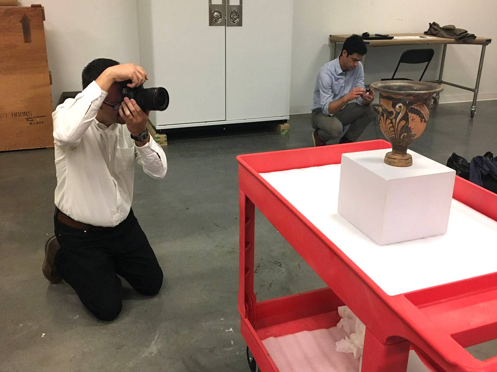 man photographing artifact on cart