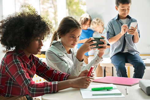Several kids seated and using their smartphones