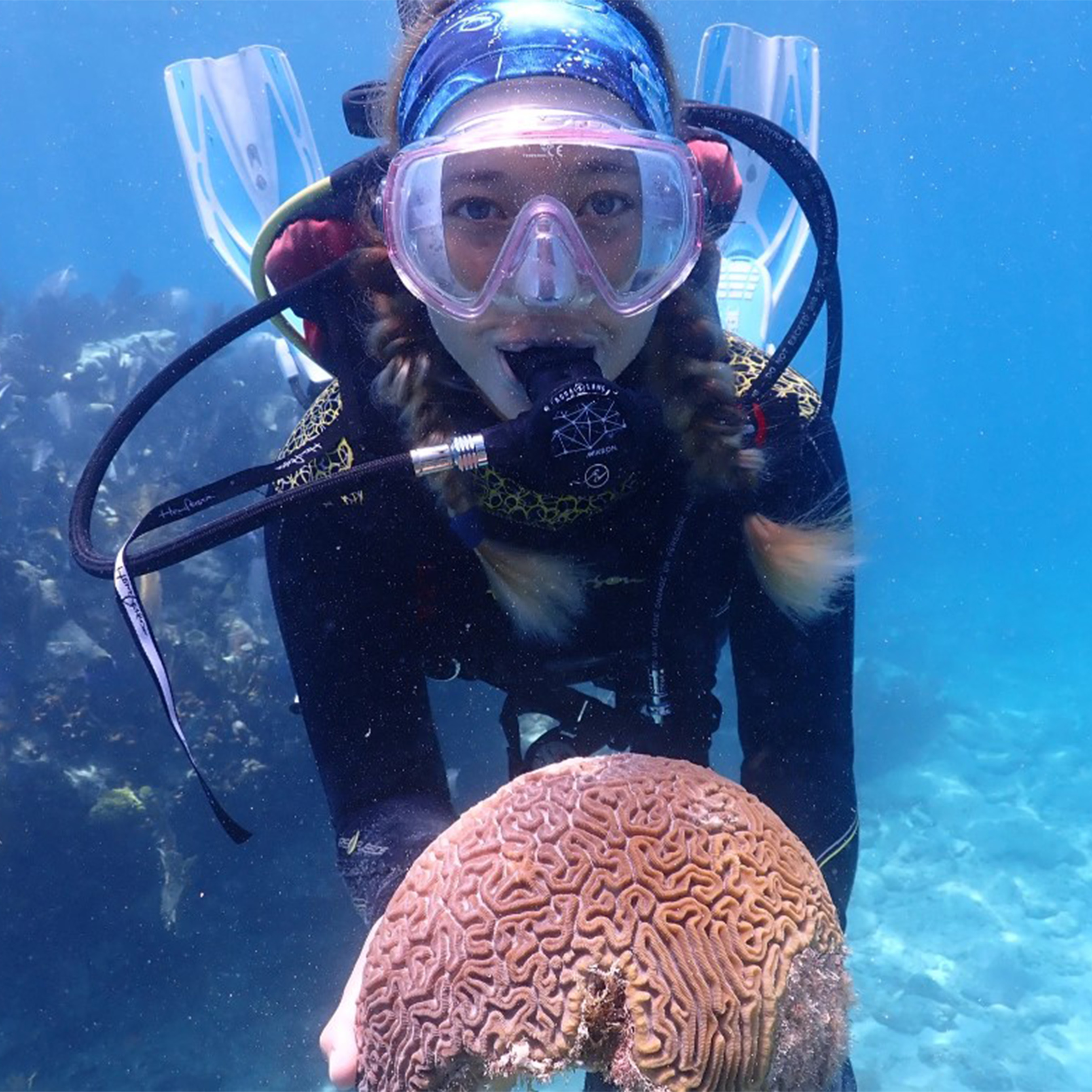 An intern in full dive gear is underwater and showing a healthy brain coral.