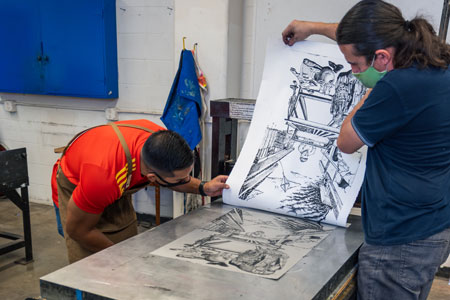 A printmaking student examines a print fresh off the press.
