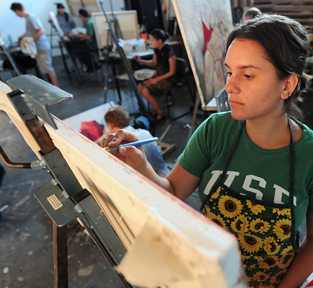 An art student focusing on her work while painting on a canvas.