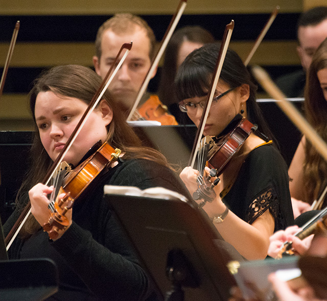 Violinists reading and playing during performance.