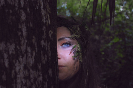 woman's face half hidden behind a tree trunk