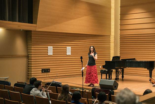 Monica Germino stands on the stage of Barness Recital Hall speaking before students
