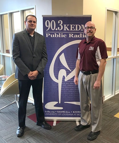 Baljinder Sekhon (left) and KEDM public radio’s Cory Crowe pose for a photo beside a KEDM sign