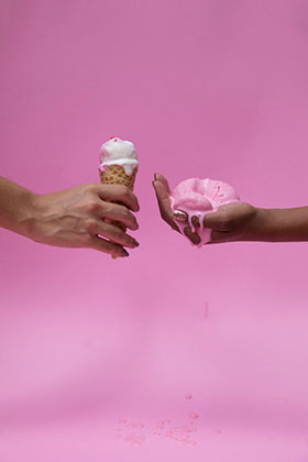 "Protraction" by Erika Schnur, former USF BFA student. Two hands holding melting icecream against a pink background.