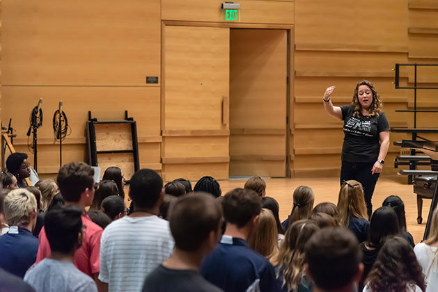 Ruthie Nelson stands on stage working with AVoice4Peace singers at the USF Concert Hall