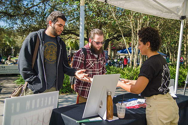 Two students interact with Marty De La Cruz, a member of USF CAM Club, at the club's table at Bull Market