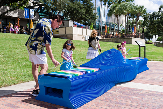 A man and a young girl play The Urban Conga's marimba bench outside the Straz Center in Tampa, Florida