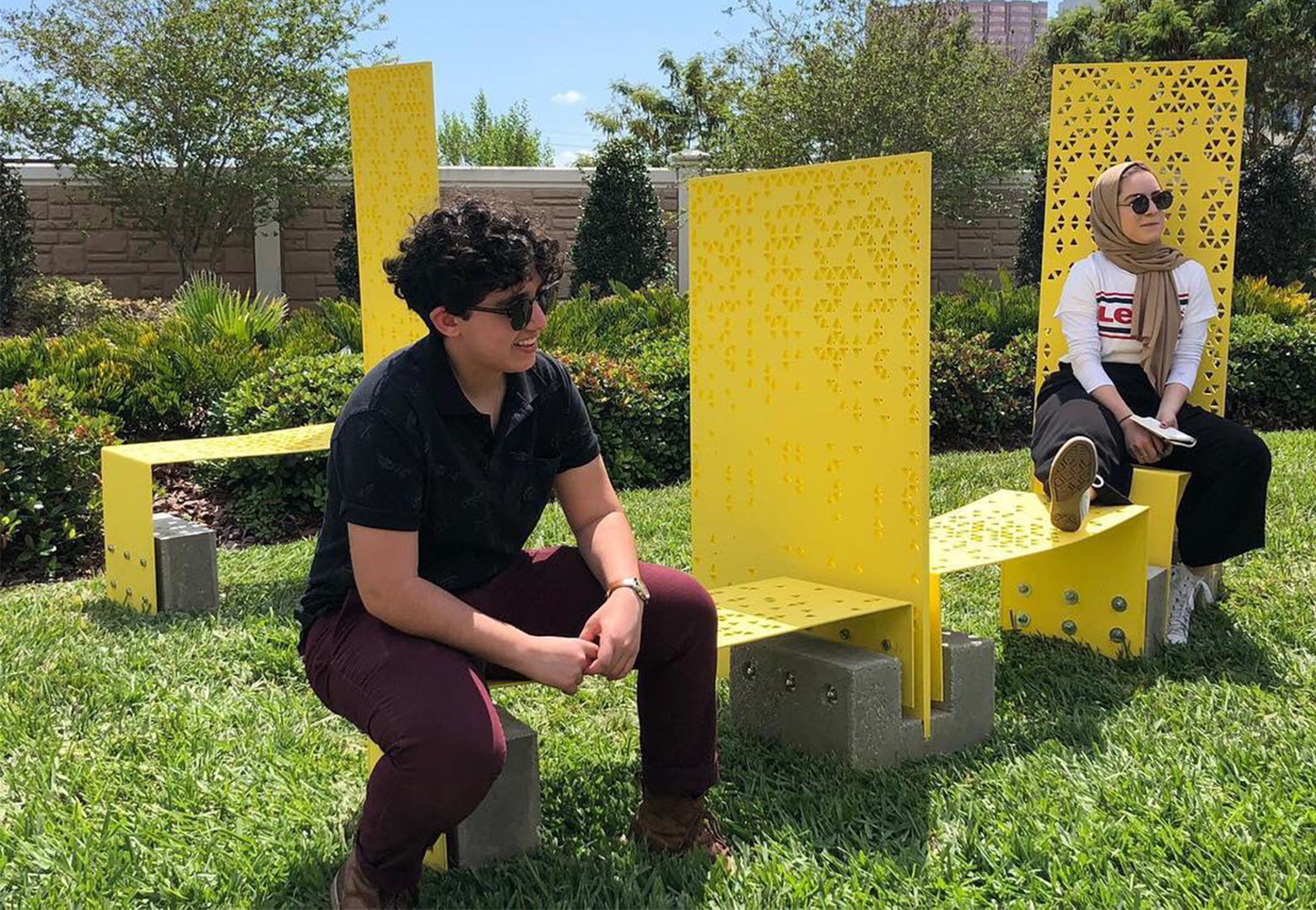 Two people sitting on a vibrant yellow piece designed by USF Architecture students for ENCORE. 