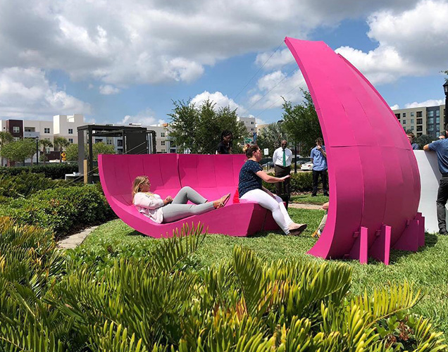 People chatting while relaxing on a bright pink curved piece made by USF Architecture students for ENCORE.