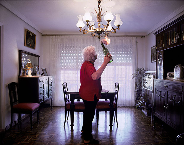 Cristina Lucas, La Anarchist (The Anarchist), 2004. An elderly woman stands with a lit molotov cocktail in hand in a dining room.