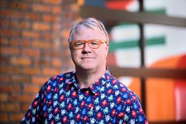 headshot of Damon Caldwell wearing colorful shirt with printed robots