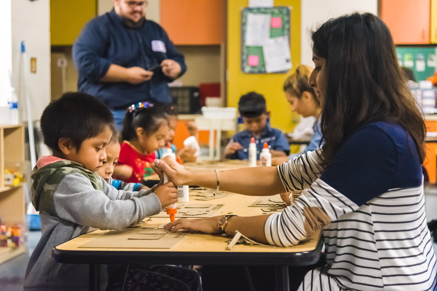 USF architecture student helps a VPK student use a bottle of glue while he works on his house design.