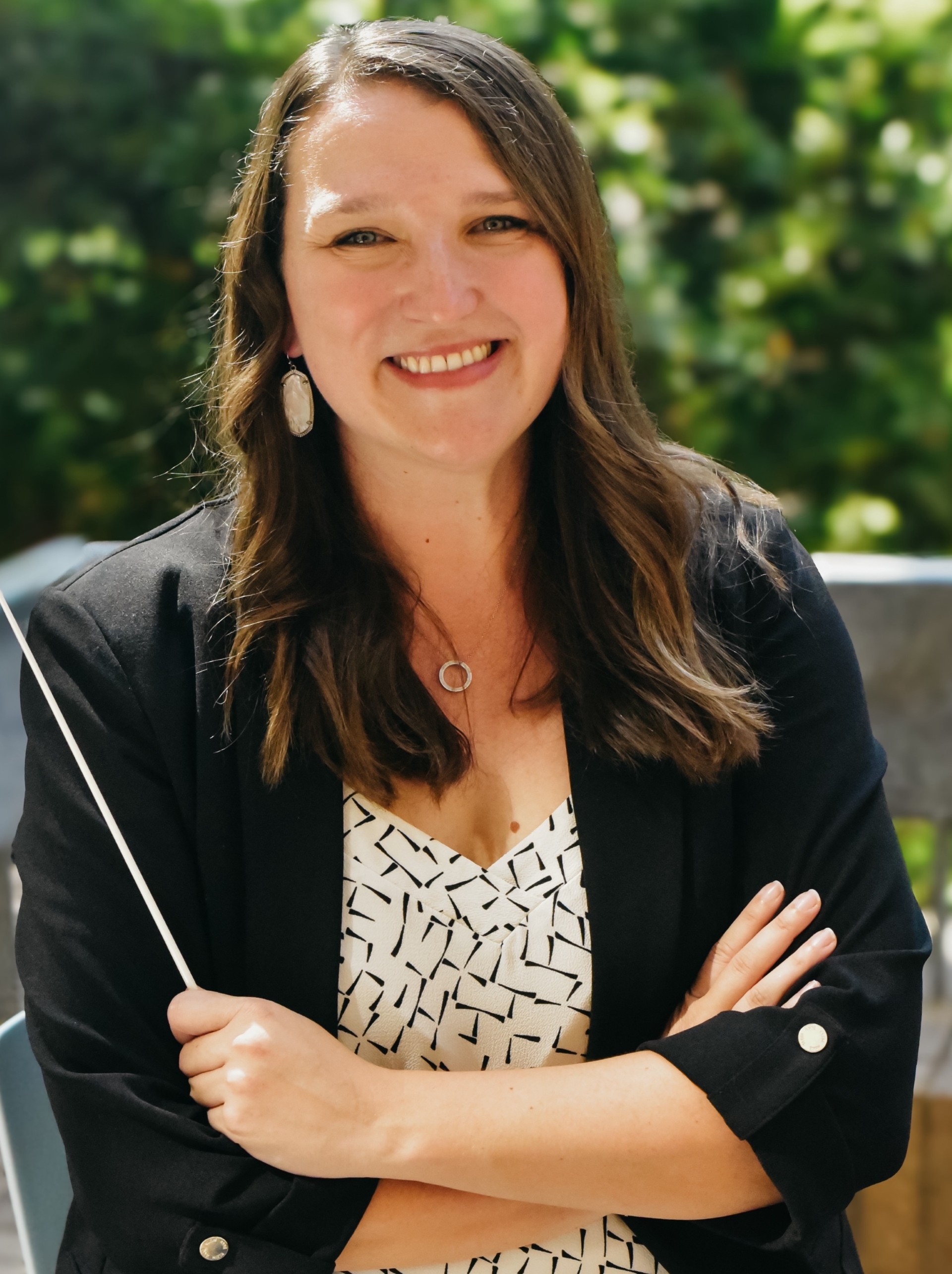 Suzanne Charney wearing a black and white shirt and a black blazer holding a conducting baton.