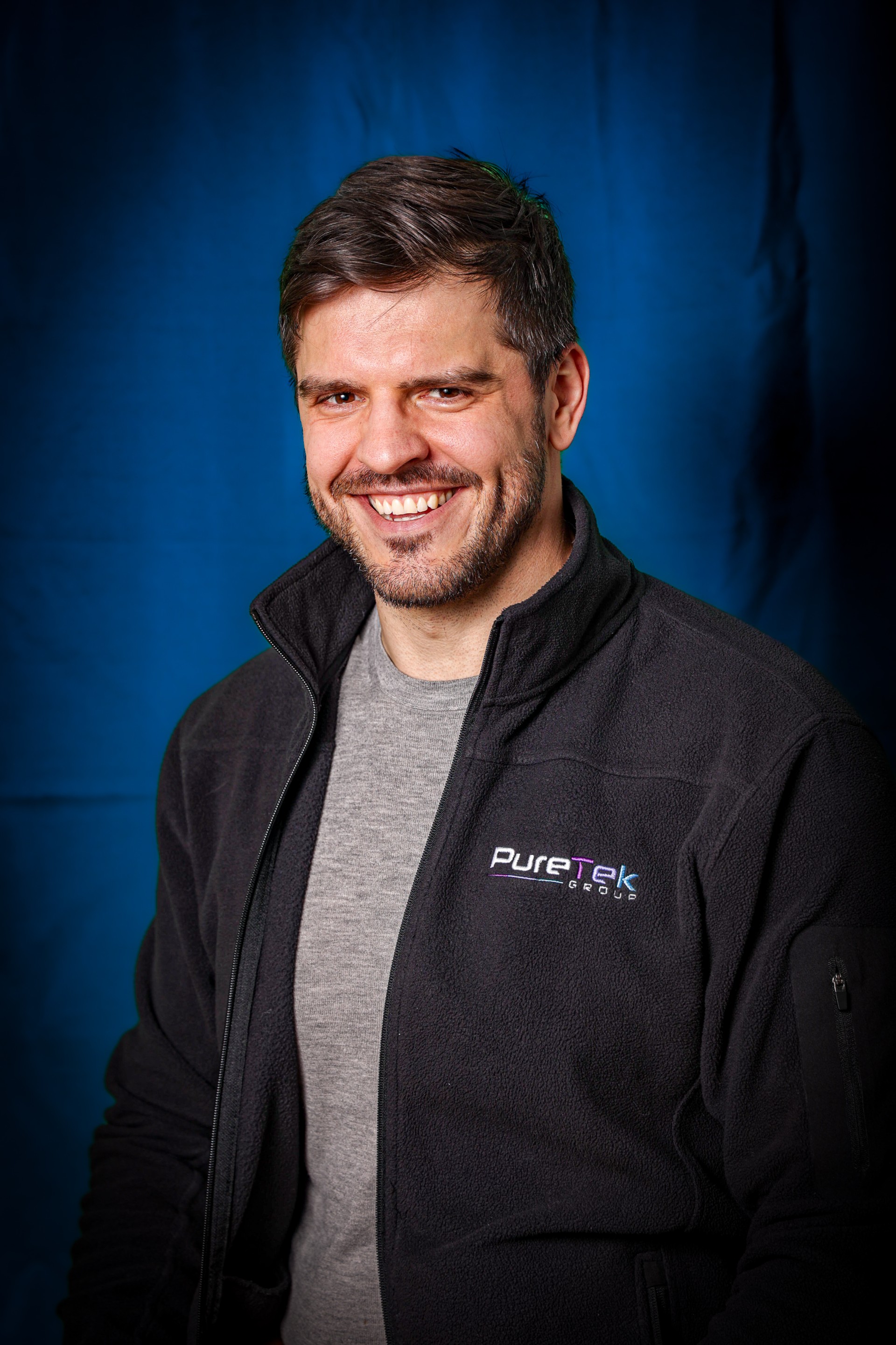 Evgeny Milov wearing a grey t-shirt and black fleece jacket in front of a blue background