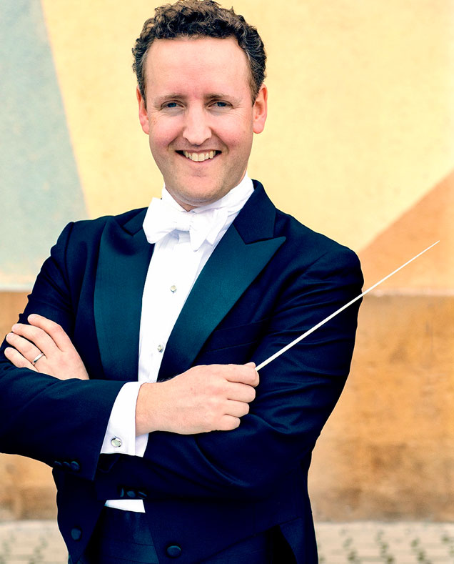 Michael Francis wearing a tuxedo and holding a conducting baton