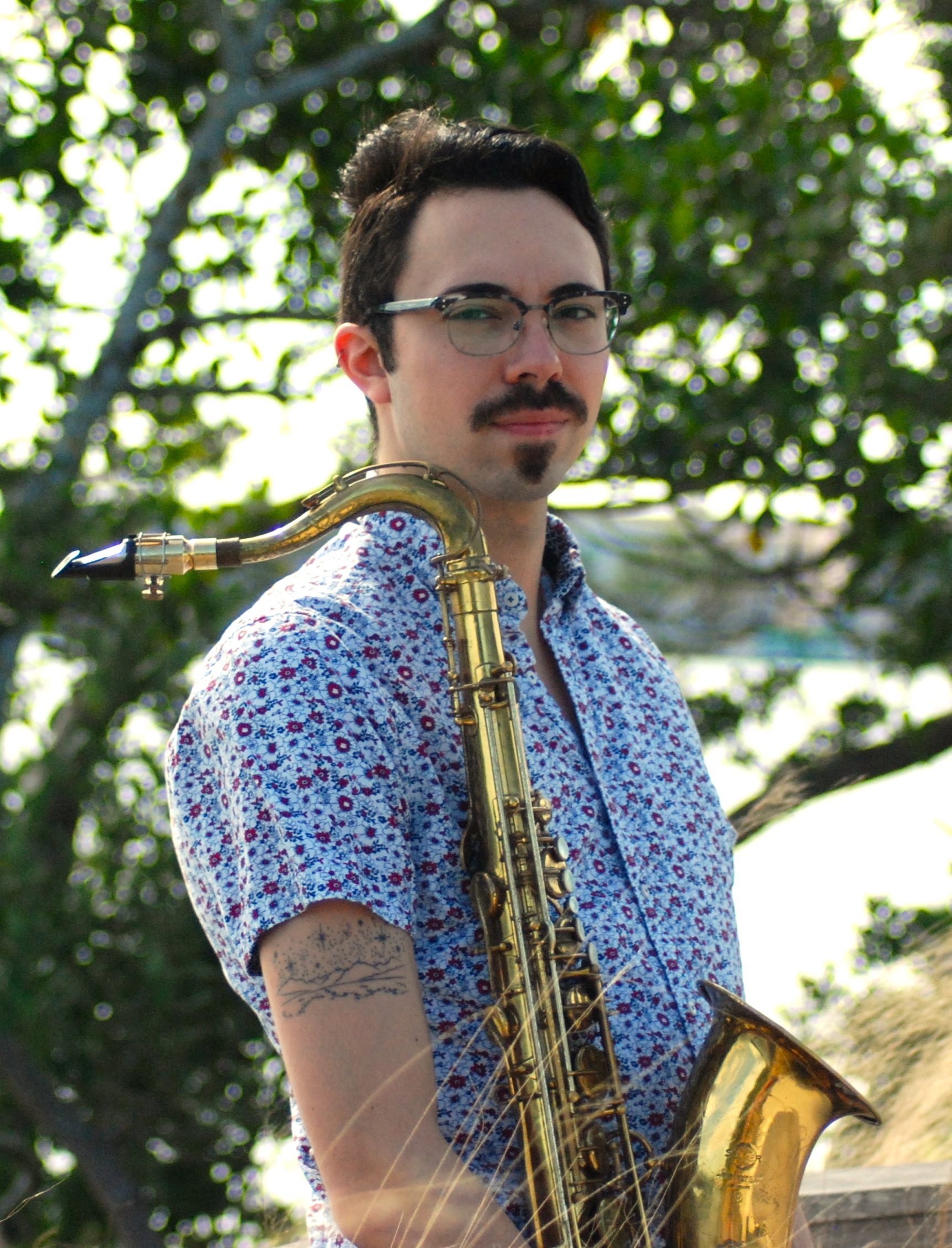 Ross Strauser holding a saxophone wearing a patterned collared shirt