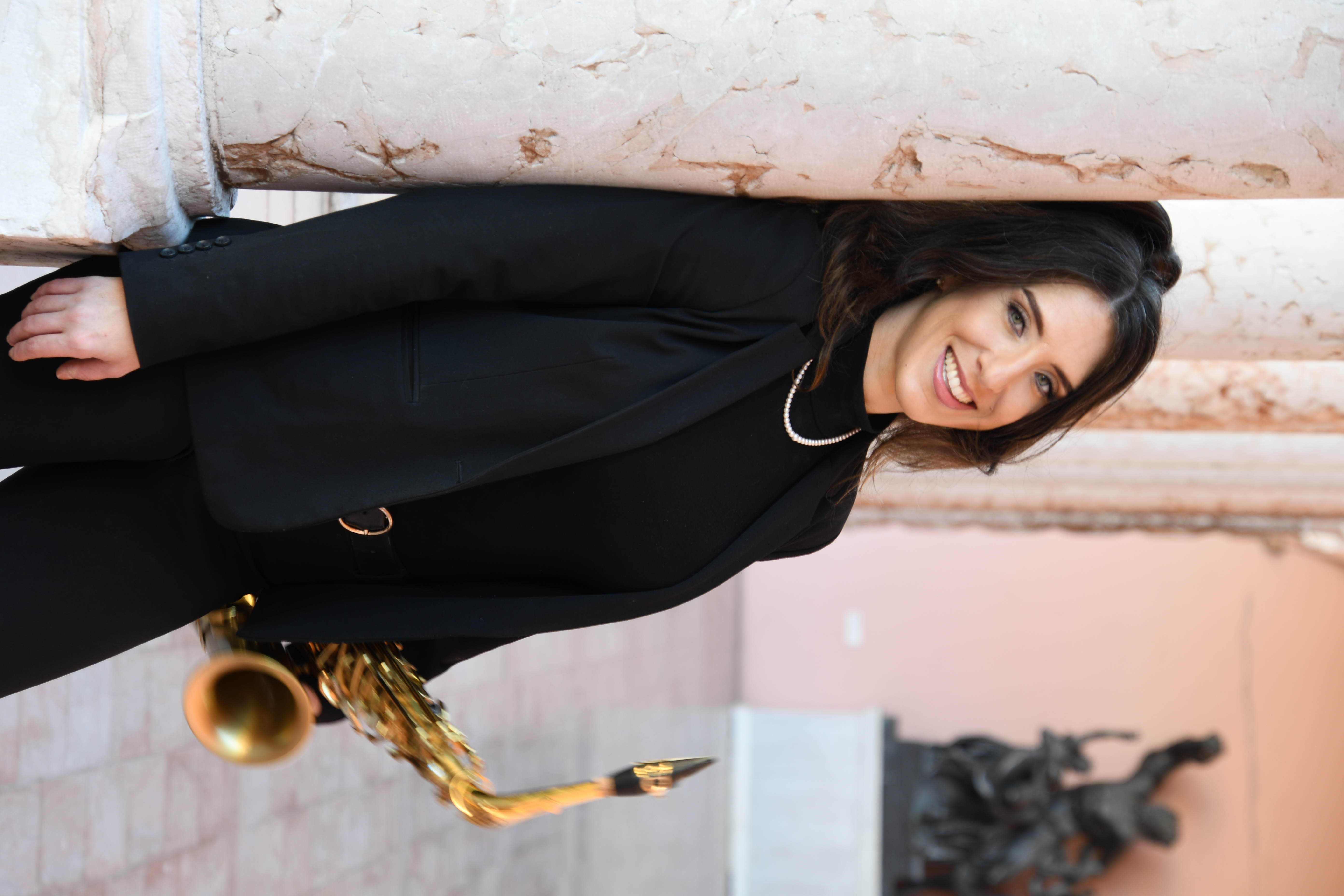Dr. Weintraub-Pearce holding a saxophone and leaning against a pillar.