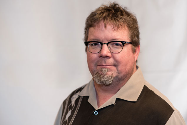 Headshot image of Tom Brantley wearing a tan and brown collared shirt in front of a white background.