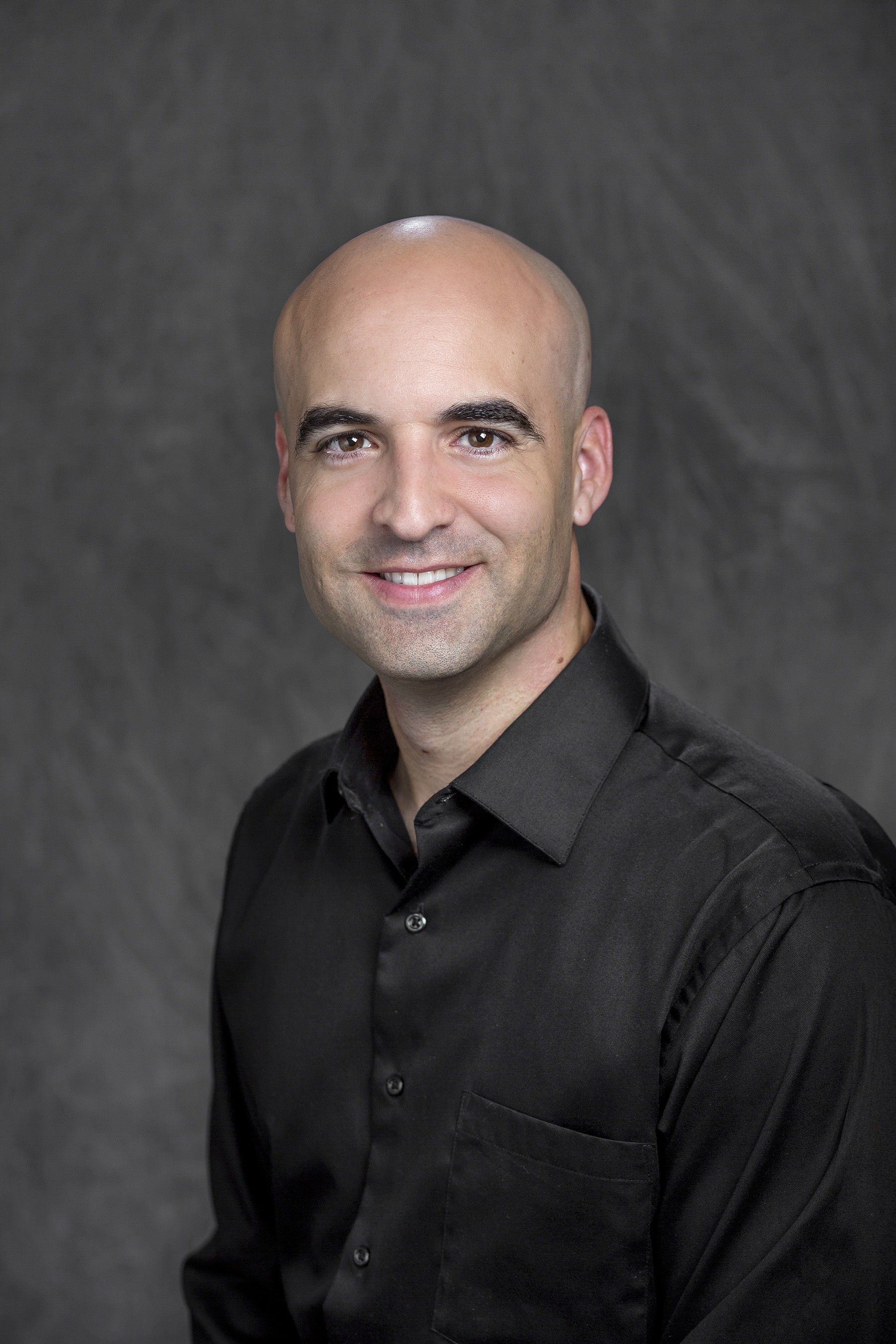 Headshot image of Dennis Llinas wearing a black collared shirt in front of a gray background.