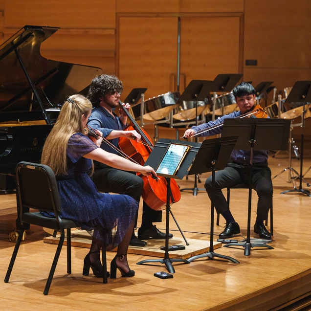Three students perform strings on stage at the Peter and Cynthia Zinober Concert Hall