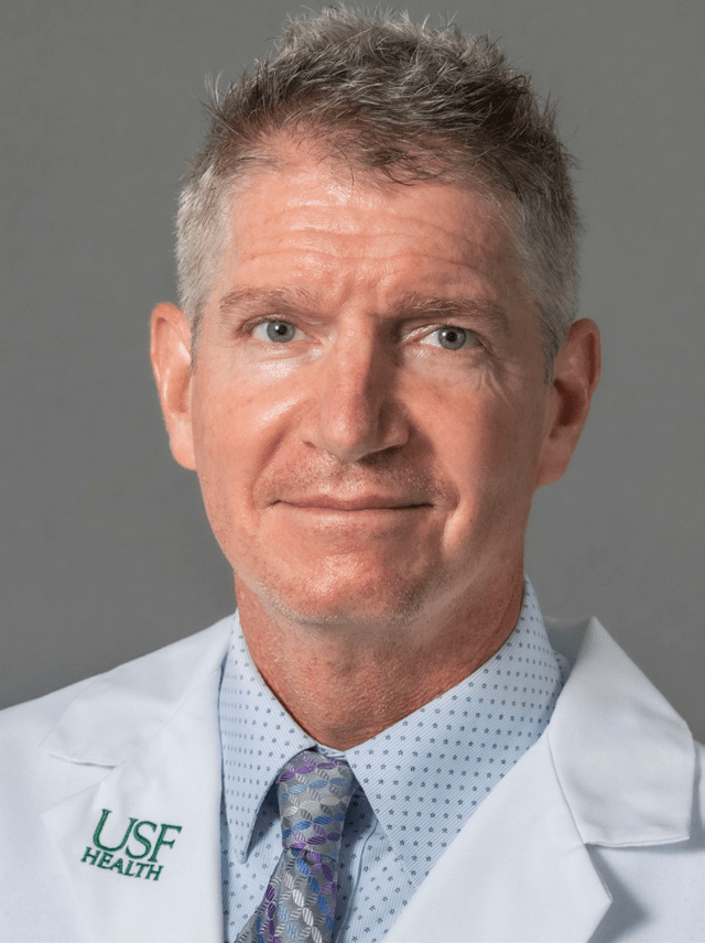 Eric Coris wearing a medical coat, polka dotted shirt and patterned tie.