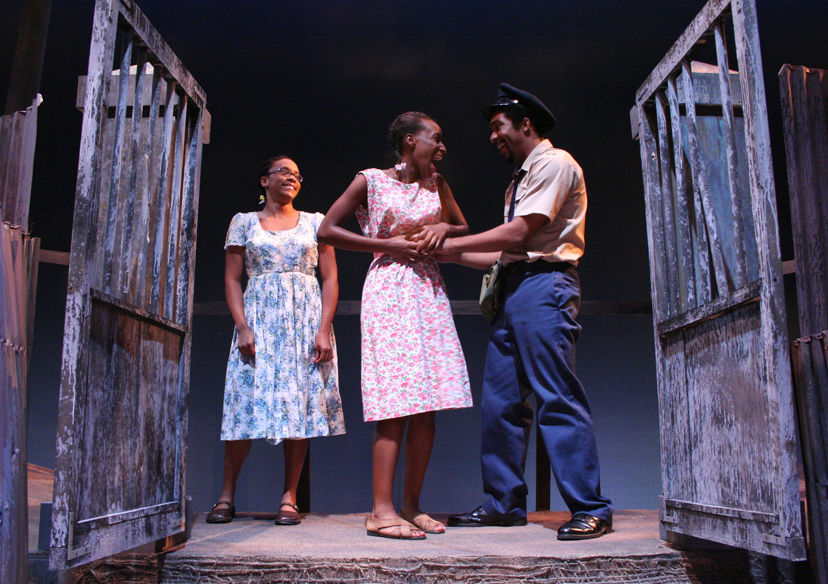 A man dressed as a police officer and a woman are exclaiming excitedly in a happy way as they have both of their hands clasped together tightly on a woman’s abdomen. Another girl stands aside near them smiling. 