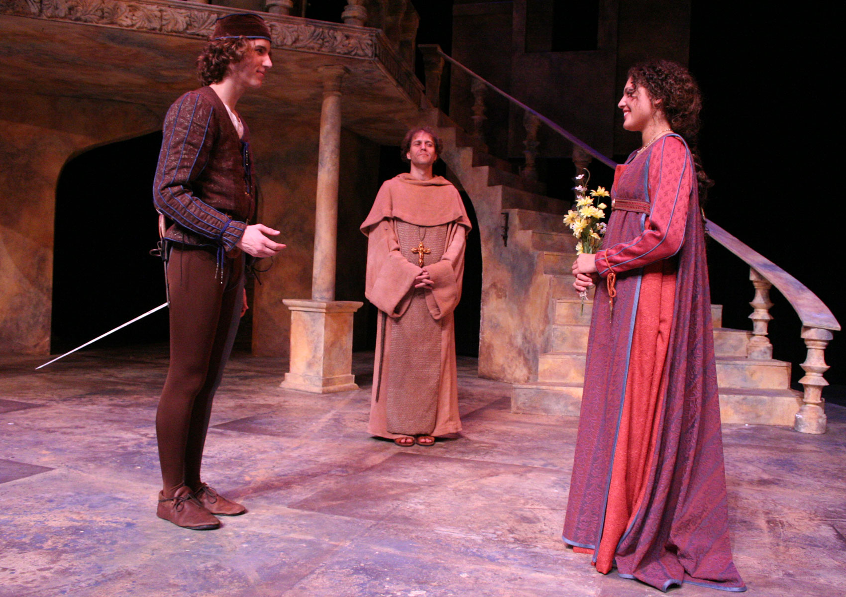 A man and a woman smile at each other while a man in friar attire watches them from behind.