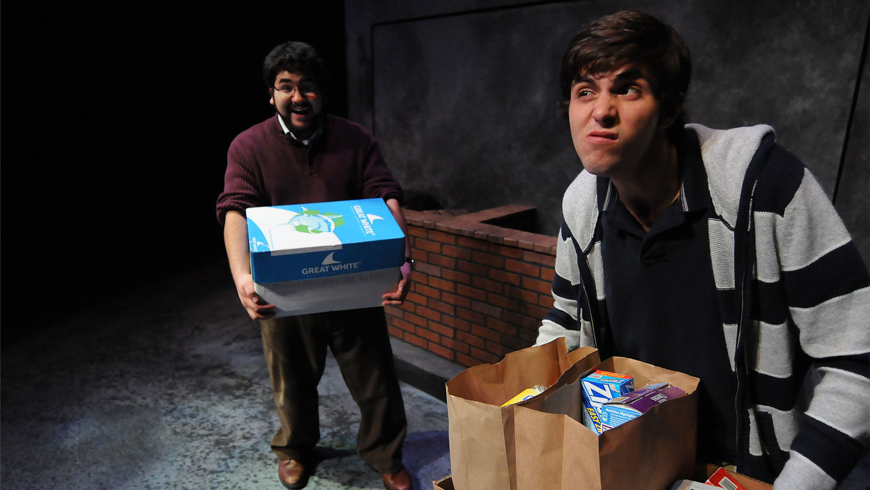 A man smiling and holding a box with a boy holding grocery bags