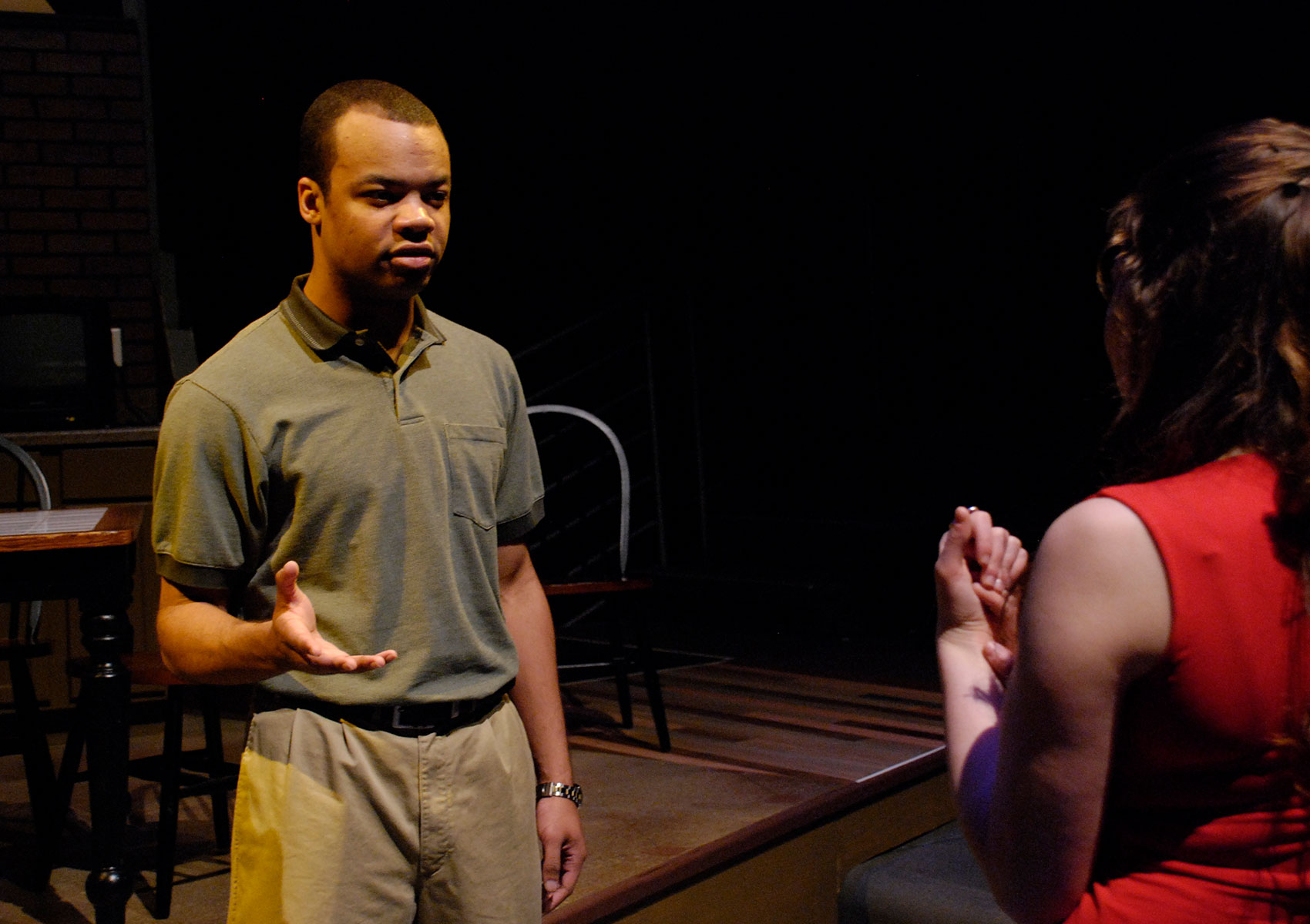 A man is talking to a woman with his palm outstretched. The woman has her hand folded with her fingers pressed lightly against her palm and her thumb on her wrist. 