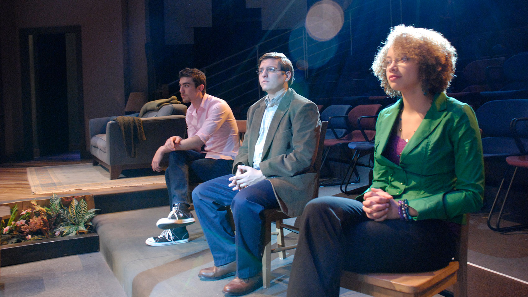 Three characters sit next to each other in a line on wooden chairs.