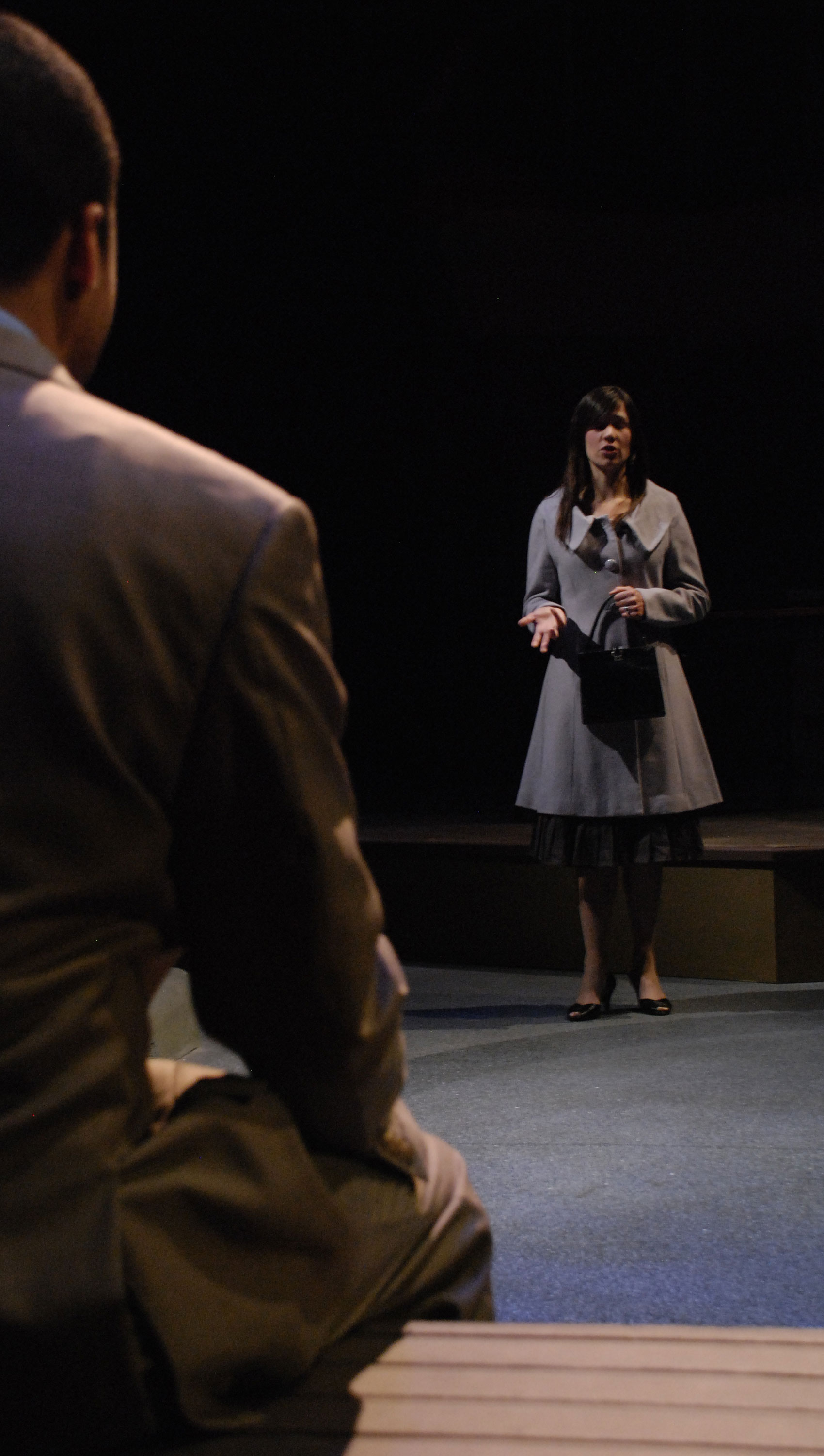 A woman is talking to a man, one hand outstretched. The man is sitting with his back facing the camera.