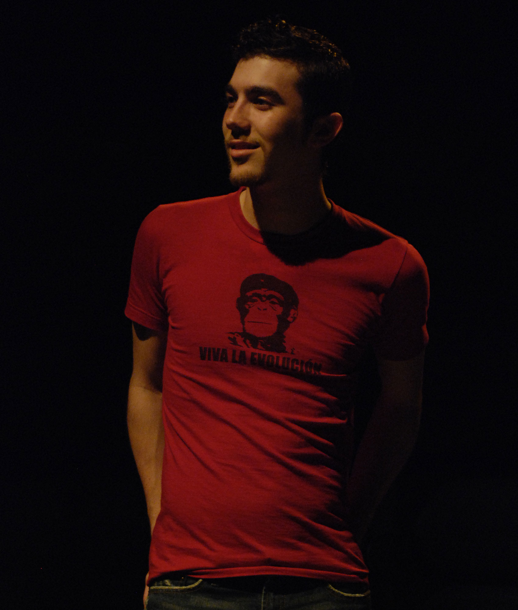 A man stands with a half-smirk on his face wearing a t-shirt that says “VIVA LA EVOLUCIÓN”.