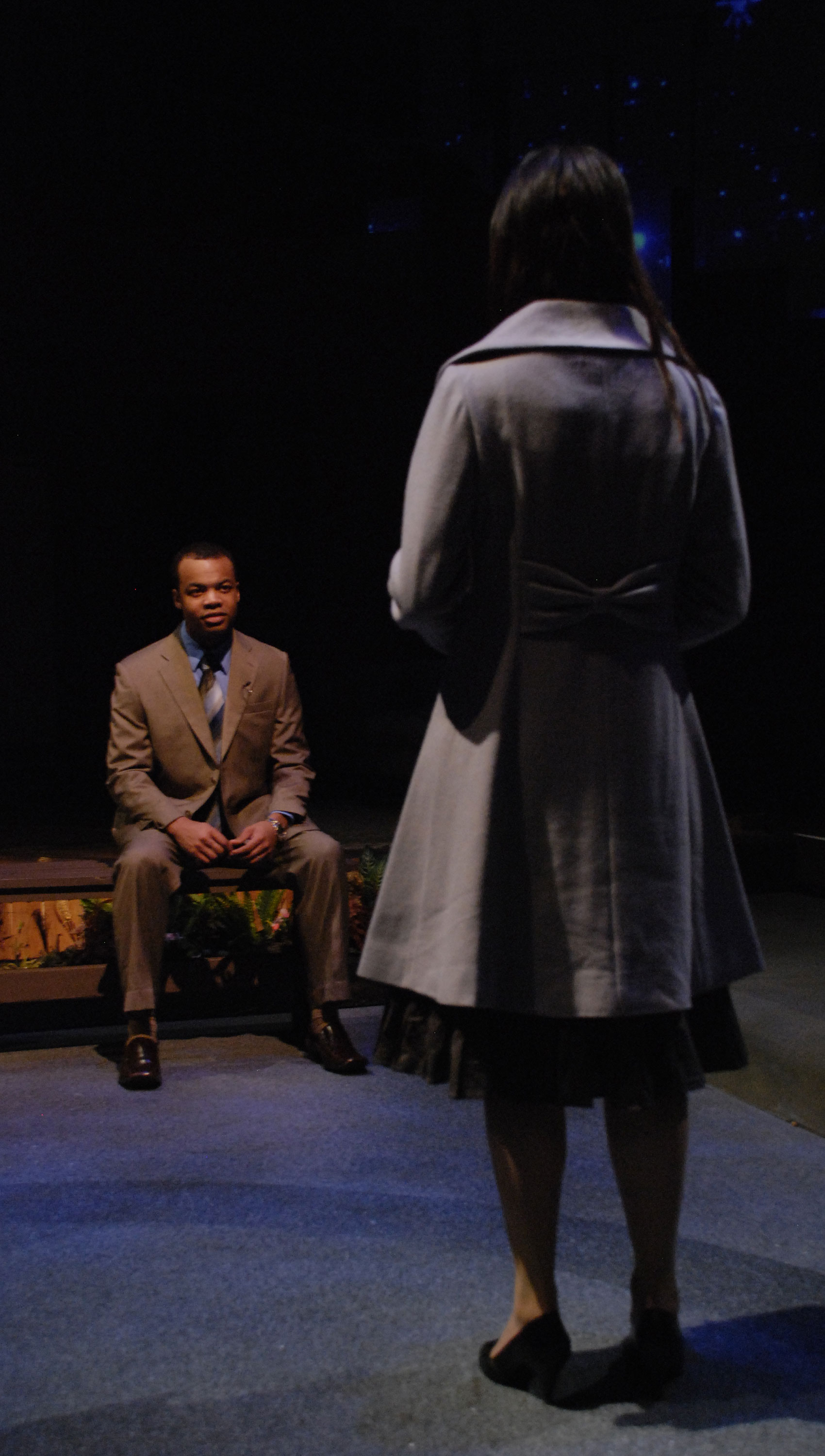 A man sits on a bench in front of a woman.