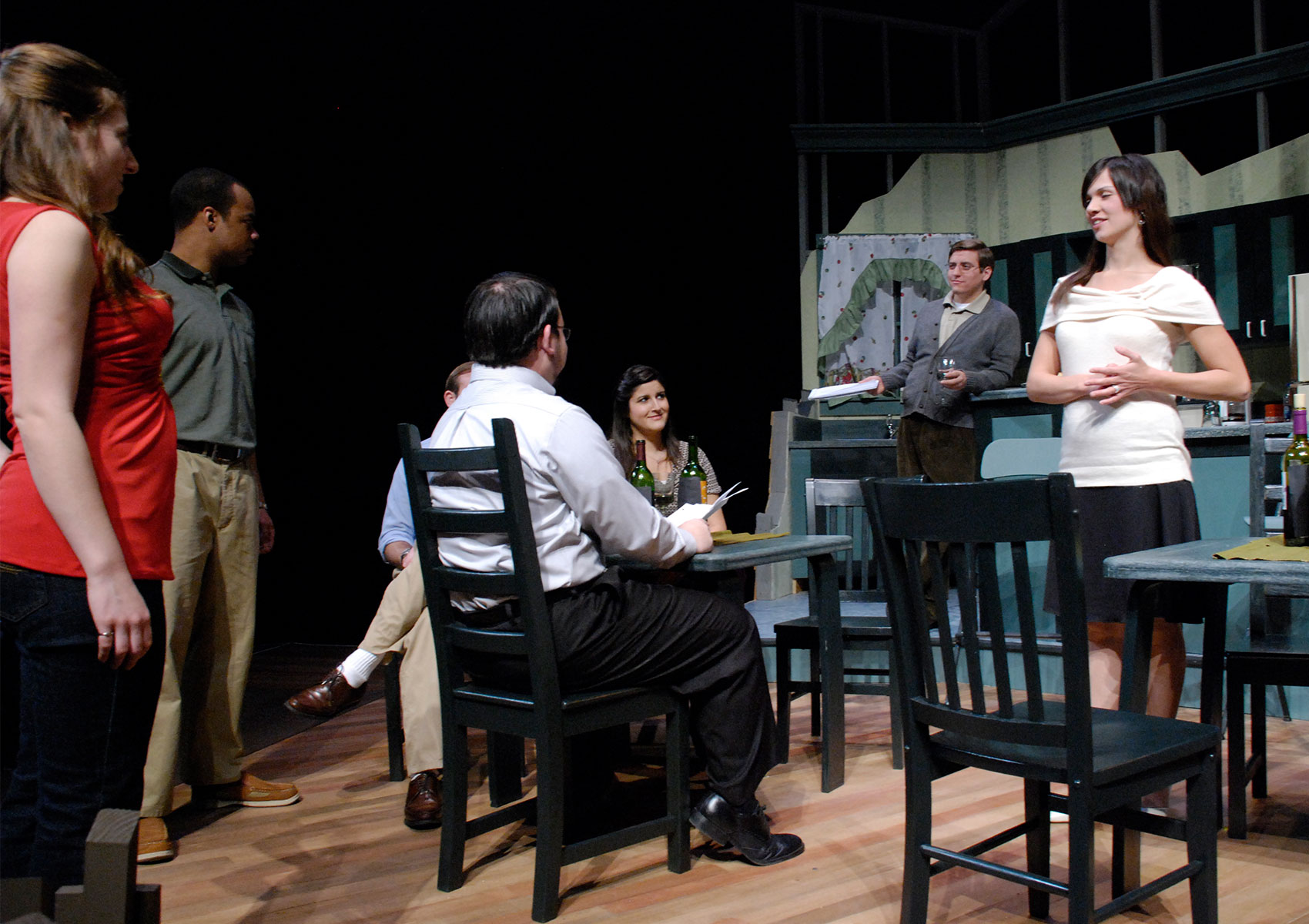 A group of characters surround a kitchen table in conversation.